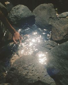 someone is holding sparklers in their hand near some rocks and water on the ground