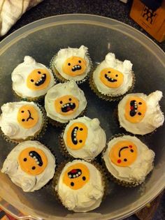 twelve cupcakes with smiley faces on them sitting in a glass bowl next to a knife