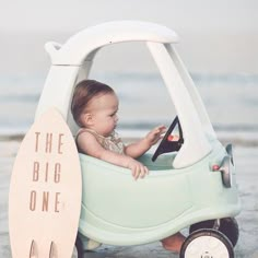 a baby sitting in a toy car on the beach