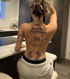 a woman with tattoos on her back sitting in a bathroom