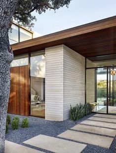 a modern house with wood and glass on the front door, along with stone steps leading up to it