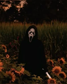 a person in a black hoodie with a white mask on standing in a field of sunflowers