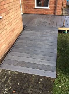 a wooden deck in front of a brick building with grass growing on the ground next to it