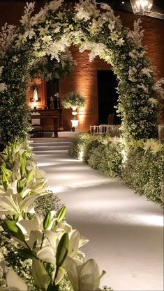 an archway with white flowers and greenery in front of a brick building at night