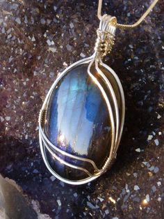 a pendant with a large blue stone in the center on a granite surface next to a rock