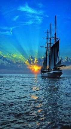 a sailboat in the ocean at sunset with clouds and sunbeams behind it