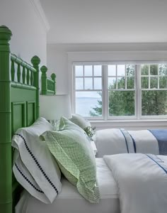 a bed with white sheets and green headboard in a bedroom next to a window