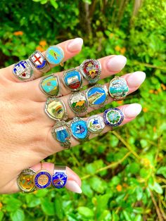 a woman's hand with several rings on it and green plants in the background