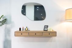 a wooden shelf with two drawers underneath a mirror on the wall next to a lamp