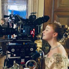 a woman is standing in front of a camera set up for a scene with other people