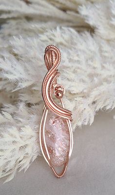 a wire wrapped pendant with a pink stone in the center on top of some white feathers