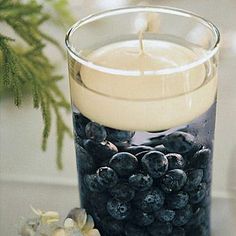 a candle with blueberries in it sitting on a table next to a vase filled with flowers