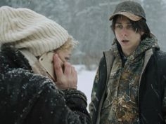 two people standing in the snow talking on their cell phones and one is holding a phone up to his ear