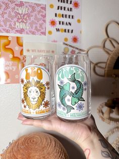 someone holding two glasses in their hand with different designs on the glass and one has a fish