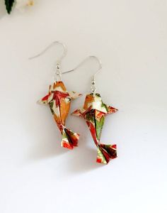 pair of origami fish earrings on white surface with flowers in the back ground