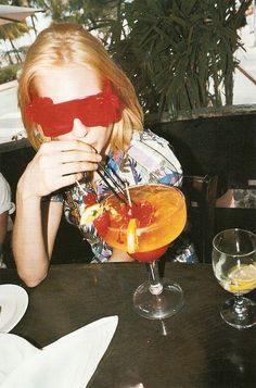 a woman wearing red glasses sitting at a table with a drink in front of her