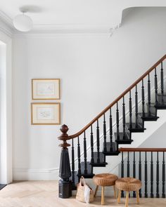 a staircase with two stools next to it and pictures on the wall