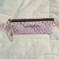 a pink and white monogrammed pencil case with zippers on the inside, sitting on a bed