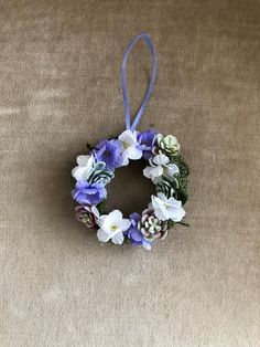 a wreath with purple and white flowers hanging on a tan carpeted wall next to a blue ribbon