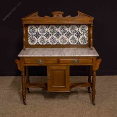 an old wooden desk with marble top and drawers on it's legs, in front of a black wall