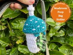 a crocheted blue mushroom poop bag holder hanging from a tree with leaves in the background