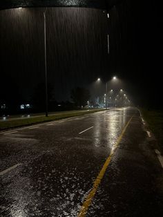 an empty street at night with the lights on and rain coming down from the sky