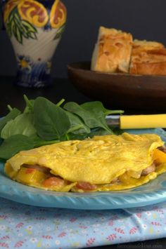 an omelet on a blue plate with spinach and bread in the background