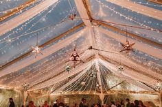 the inside of a tent with lights and stars hanging from it's ceiling is filled with people