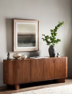 a wooden sideboard with two vases and a plant on it in front of a window