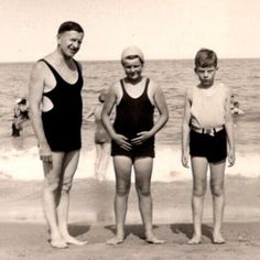 three boys standing on the beach in bathing suits and one is wearing a swim suit