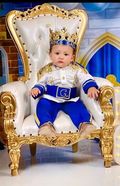 a baby sitting on top of a white chair wearing a blue and gold suit with a crown