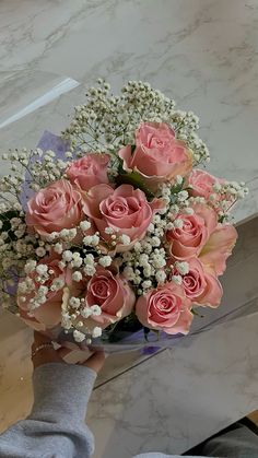 a bouquet of pink roses and baby's breath is being held by a person