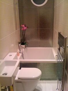 a white toilet sitting next to a bath tub in a bathroom under a window with a circular mirror above it