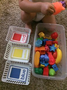 a baby sitting on the floor with some toys in it's hands and an empty container