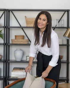 a woman standing in front of a book shelf with a bag on top of it