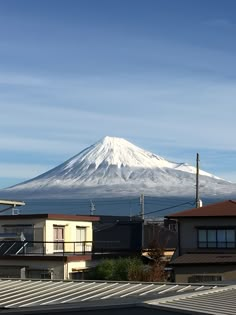 a snow covered mountain is in the distance behind some houses and rooftops on a sunny day