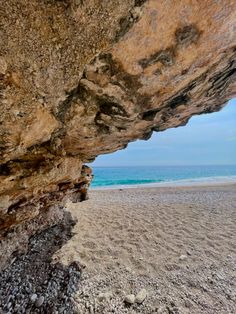 the beach is covered in large rocks and sand, as seen from under an overhang