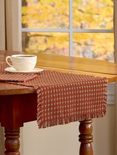 a wooden table topped with a cup and saucer on top of it next to a window