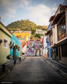 an empty street with colorful buildings and graffiti on the walls, in front of a mountain