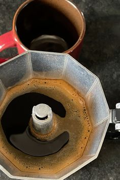 an upside down coffee pot sitting on top of a counter next to a red cup