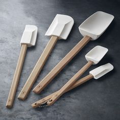 five wooden utensils with white handles on a gray surface, including one spoon and two spatulas