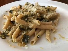 a white plate topped with pasta covered in pesto and parmesan toppings