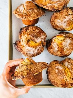 a person holding a muffin in front of some other muffins on a tray