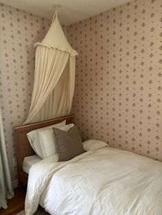 a white bed sitting in a bedroom next to a wall papered with floral designs