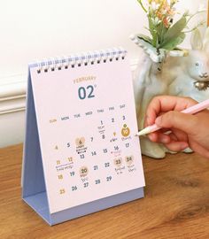 a person is writing on a calendar next to a small bunny figurine and flowers