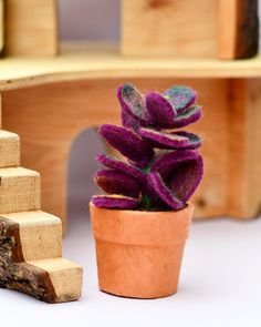 a small potted plant sitting next to a wooden stair case with purple flowers in it