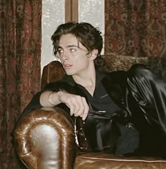 a young man sitting on top of a brown leather chair in front of a window