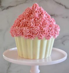 a cupcake with pink frosting sitting on top of a white cake platter