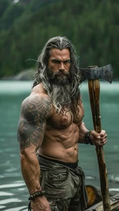 a man with long grey hair and beard holding an ax in his hand while standing next to a body of water