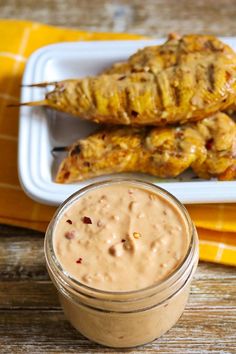 grilled chicken skewers with peanut butter sauce on a white plate next to a yellow napkin